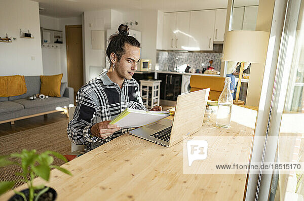 Young man with document working on laptop at home office
