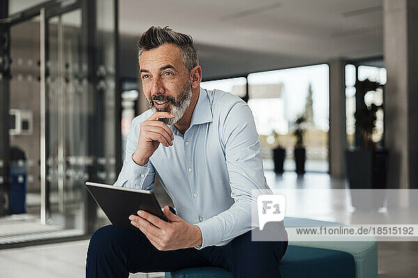 Thoughtful businessman sitting on seat with tablet PC at office