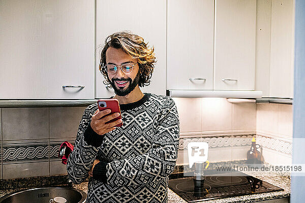 Smiling man using mobile phone in kitchen at home