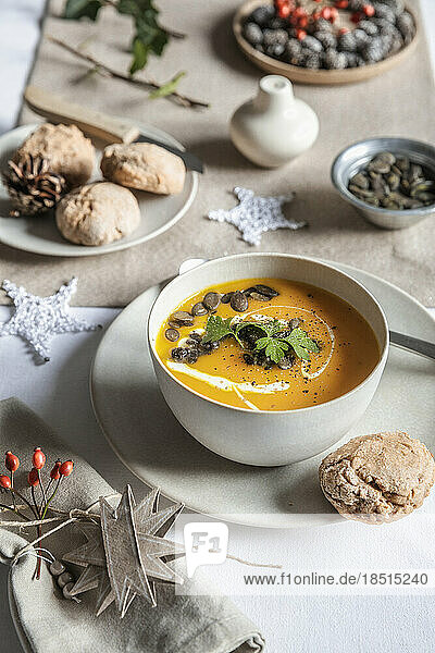 Studio shot of bowl of pumpkin soup with homemade buns in Christmas setting