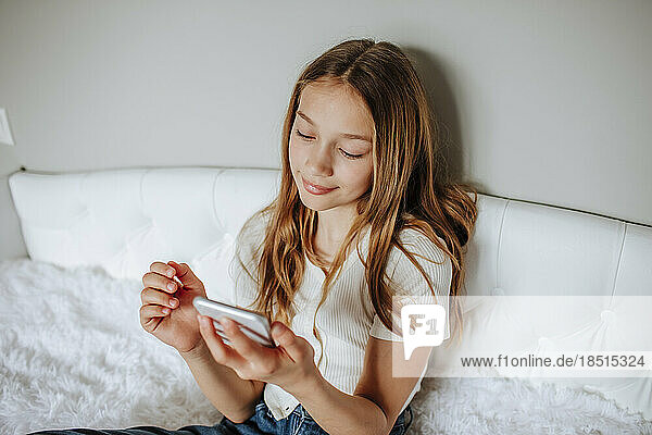 Girl using smart phone sitting on bed at home