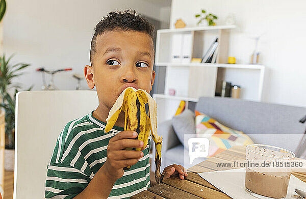 Thoughtful boy eating banana at home