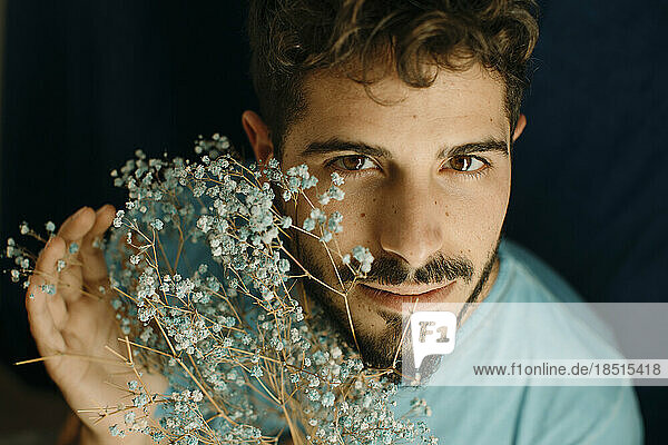 Young man with beard holding flowers against blue background