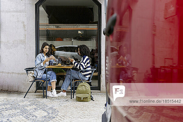 Women using smart phone sitting at table of sidewalk cafe