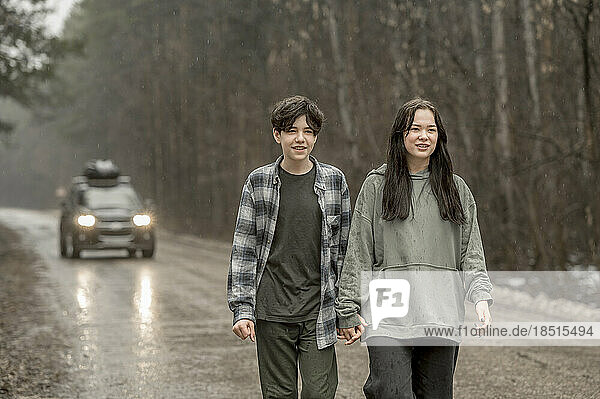 Brother and sister holding hands and walking on wet road