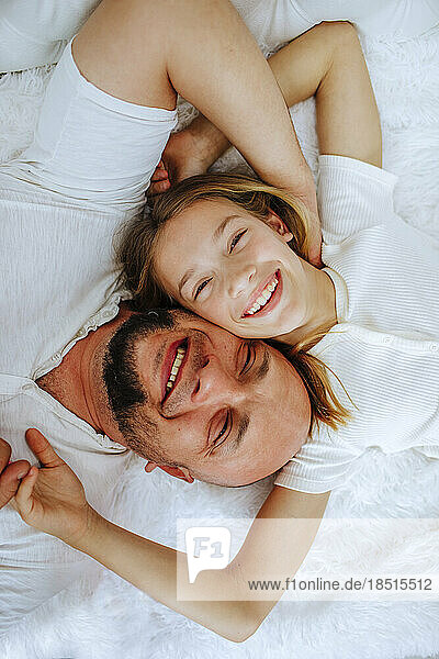 Smiling man lying down with daughter on bed at home