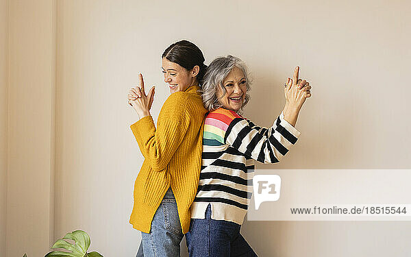 Happy mother gesturing with daughter in front of wall