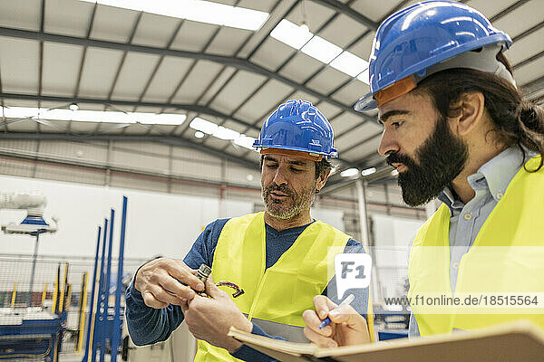 Mature engineer having discussion over machine part with colleague in industry