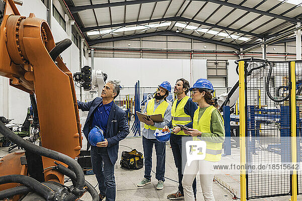 Engineer with colleagues having discussion over robotic arm