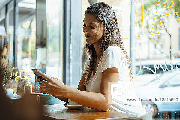 Smiling woman text messaging through smart phone in cafe