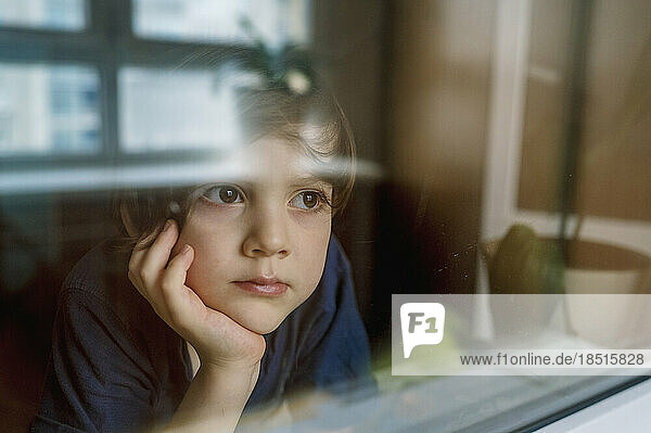 Thoughtful boy looking through glass window