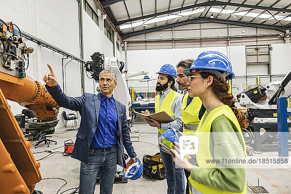 Mature engineer with colleagues having discussion over robotic arm