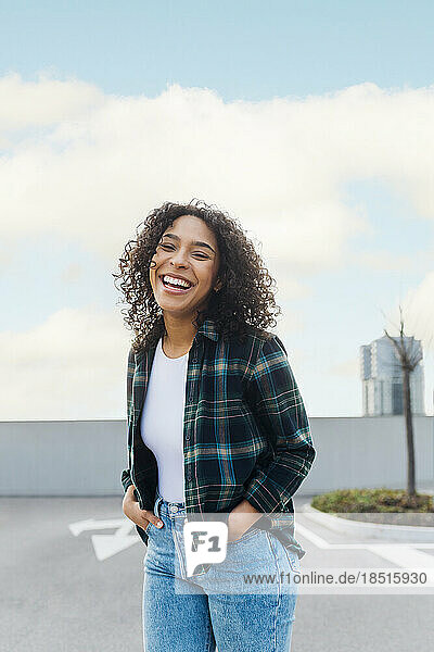 Cheerful young woman with curly hair standing on footpath