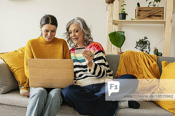 Lächelnde Tochter und Mutter kaufen online mit Kreditkarte auf dem Laptop ein
