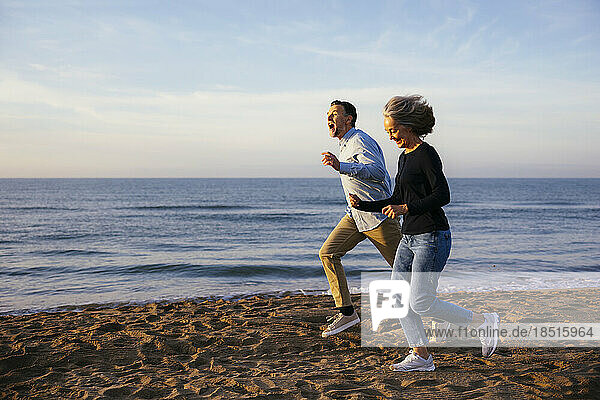 Cheerful mature man running with woman at coastline