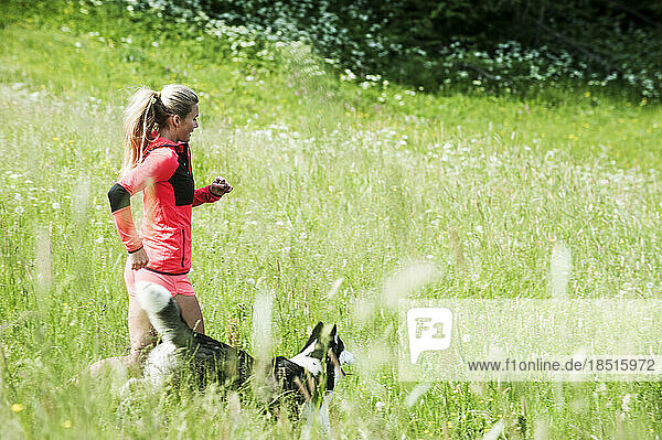 Woman running with dog in green field in sunny day