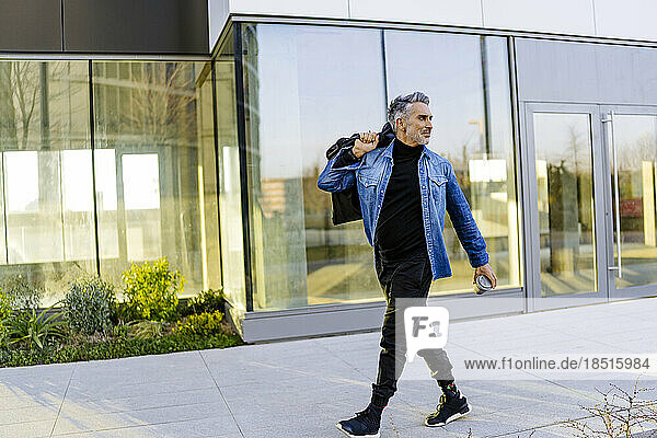 Mature man with bag and coffee cup walking on footpath