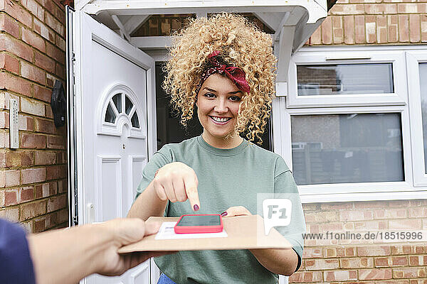 Happy woman with mobile phone taking delivery of package