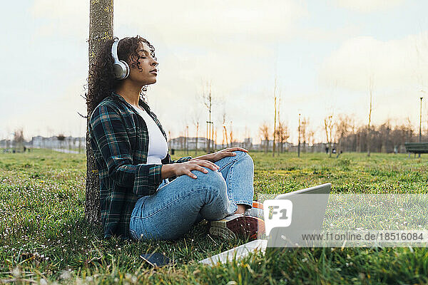 Young woman meditating by laptop at park