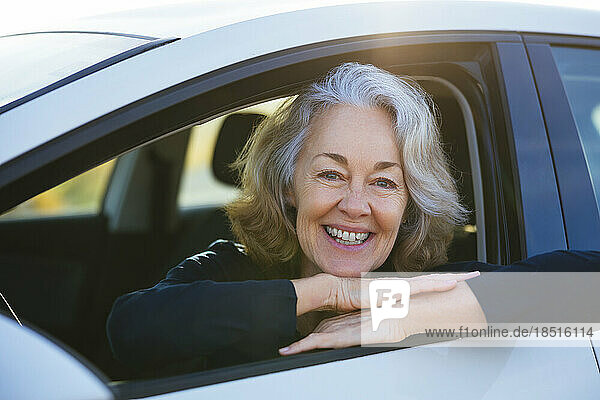 Happy mature woman leaning on car window