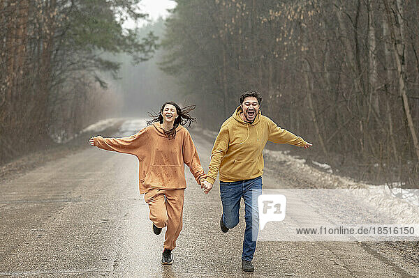 Happy couple holding hands and running on wet road
