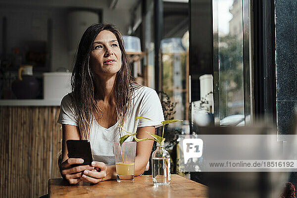 Nachdenkliche Frau sitzt mit Smartphone im Café