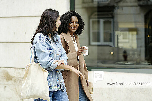 Happy young woman talking with friend and walking by building