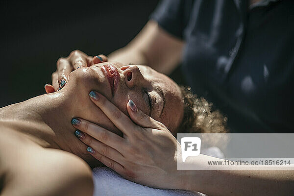 Massage therapist doing facial massage of customer at spa