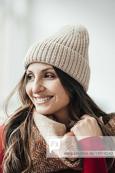 Happy woman wearing knit hat in front of wall