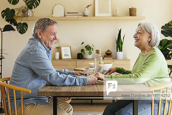 Affectionate senior couple holding hands sitting at dining table