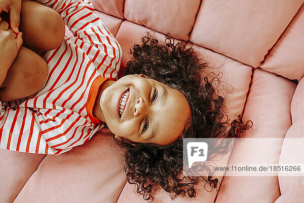 Fröhliches Mädchen  das sich zu Hause auf dem rosa Sofa amüsiert