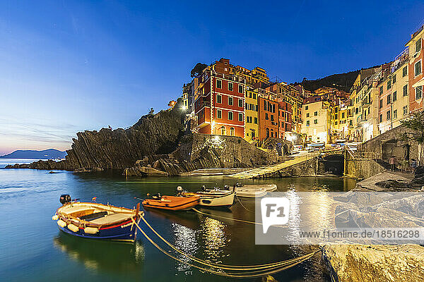 Italy  Liguria  Riomaggiore  Boats moored at edge of coastal village along Cinque Terre at dusk