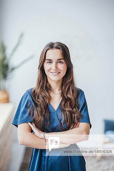 Smiling young businesswoman standing with arms crossed in office