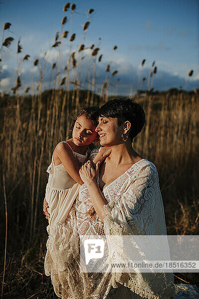 Smiling pregnant woman carrying daughter standing in field at sunset