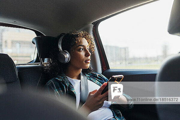 Contemplative woman with smart phone sitting in car