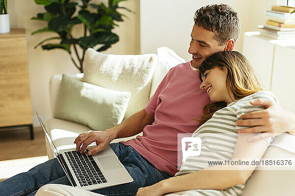 Girlfriend leaning head on boyfriend's shoulder using laptop at home