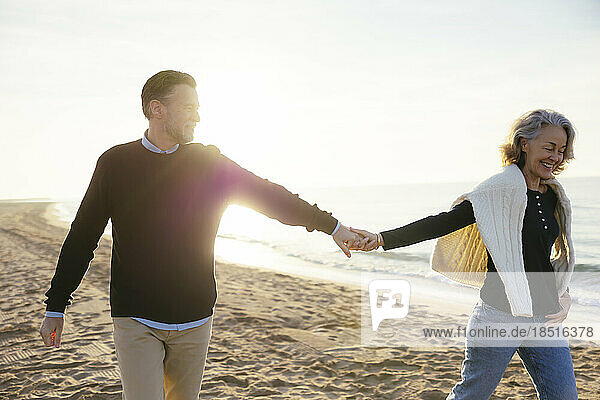 Happy woman holding hands with man and having fun at beach