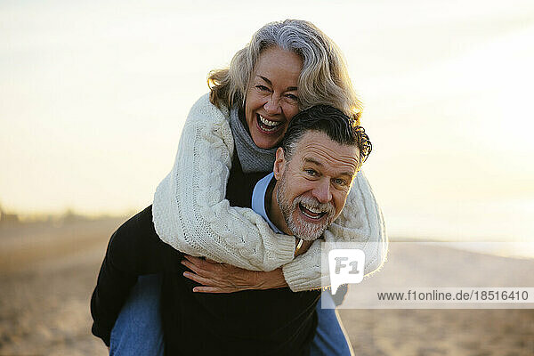 Happy mature man giving piggyback ride to woman at beach