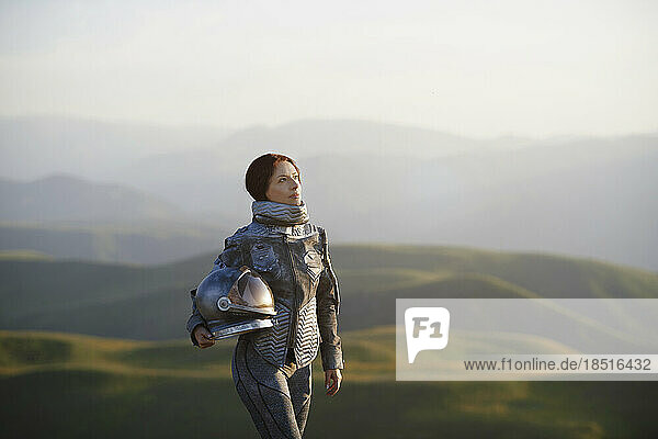 Contemplative woman with space helmet standing on landscape