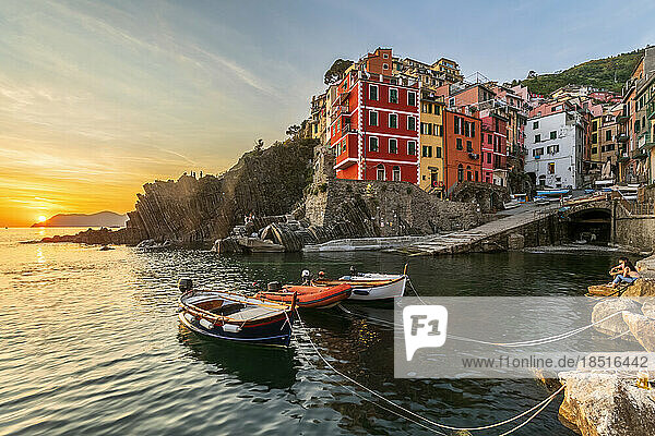 Italy  Liguria  Riomaggiore  Boats moored at edge of coastal village along Cinque Terre at sunset