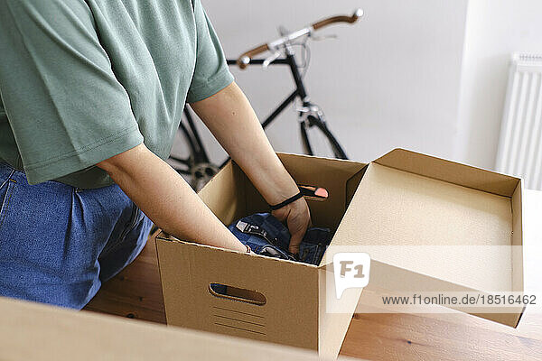 Young woman packing clothes in cardboard box