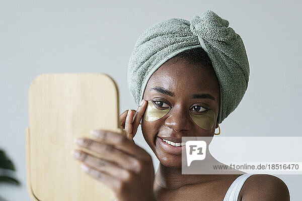 Lächelnde junge Frau mit Spiegel  die eine Augenklappe anbringt
