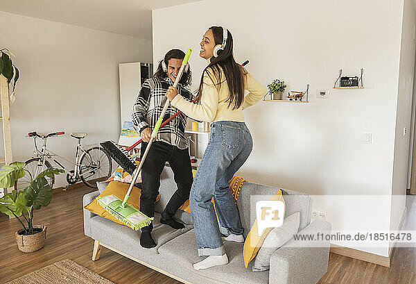 Happy couple enjoying housework standing on sofa at home