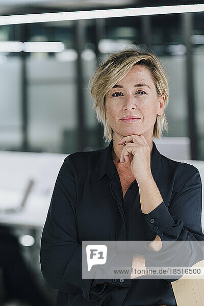 Smiling businesswoman with hand on chin in office