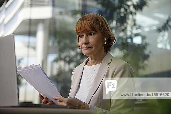 Businesswoman holding documents and looking at laptop