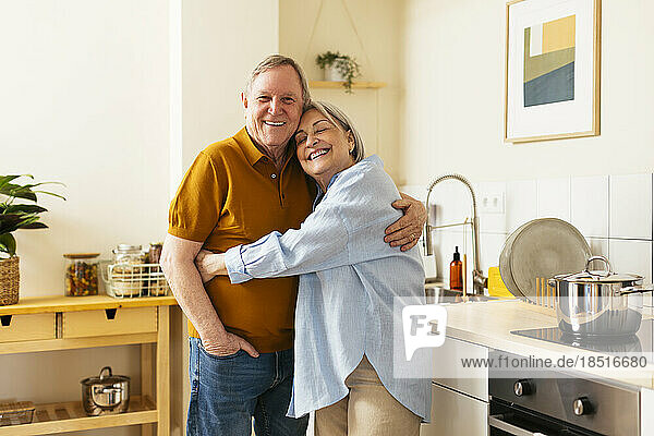 Happy senior woman embracing man in kitchen