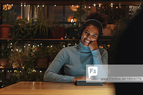 Happy businesswoman sitting with hand on chin at night in office