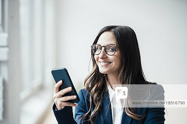 Smiling businesswoman holding smart phone at home office
