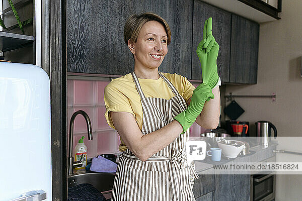 Lächelnde Frau mit Handschuhen steht in der Küche