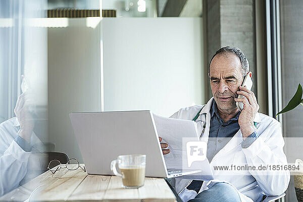 Doctor examining medical report and discussing on smart phone at desk